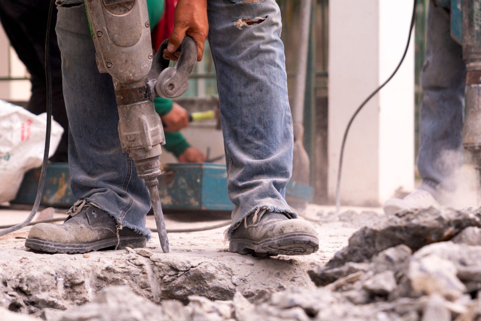 Worker using jackhammer on concrete floor.
